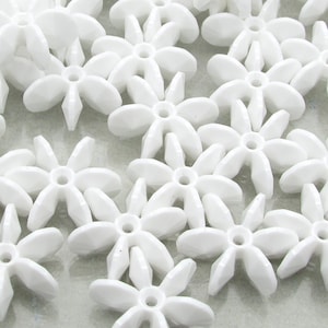 May include: A collection of white plastic flower-shaped beads. The beads have six points and a small hole in the center.
