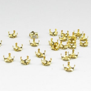 May include: A group of gold-colored metal settings for rhinestones or other small gems. The settings are shaped like crowns with multiple prongs.