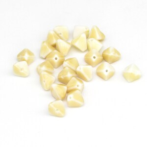 May include: A group of 18 cream-colored, faceted, pyramid-shaped beads with a hole in the center of each bead.