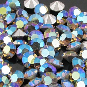 Peut inclure: Une grande quantité de strass bleu irisé et argenté. Les strass sont éparpillés sur une surface noire.