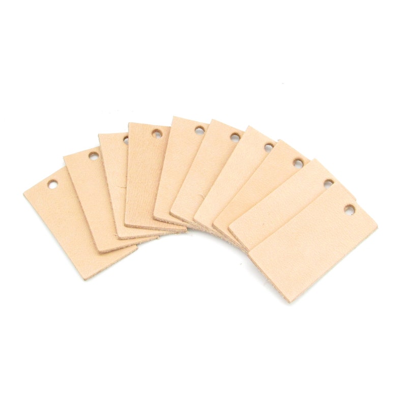 May include: Ten blank leather tags with holes punched in the top corners. The tags are a light brown color and are arranged in a fan shape.