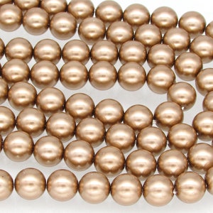 May include: A strand of round, metallic gold-colored beads. The beads are smooth and have a pearlescent finish.