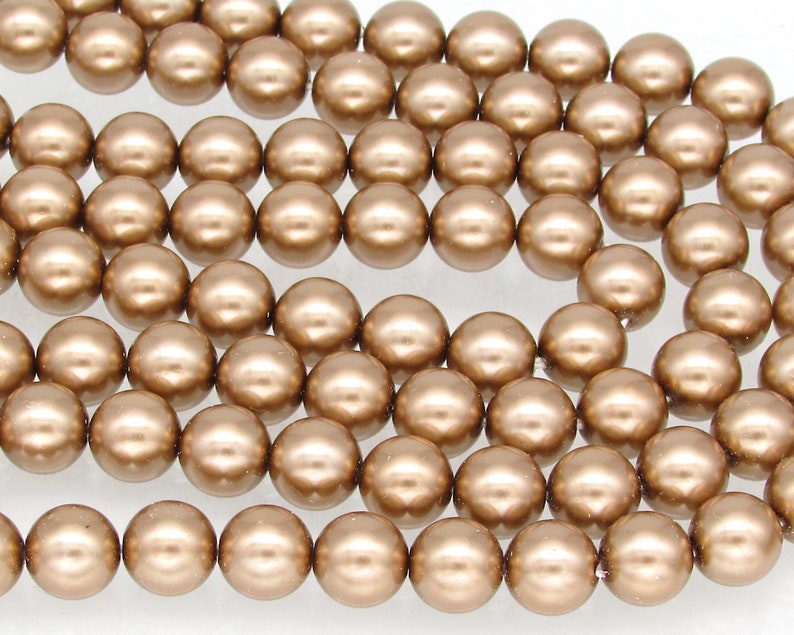 May include: A strand of round, metallic gold-colored beads. The beads are smooth and have a pearlescent finish.