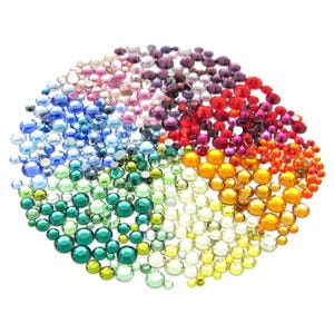 May include: A rainbow assortment of colorful rhinestones, arranged in a circular pattern. The rhinestones are small and round, with a variety of colors, including red, orange, yellow, green, blue, and purple.