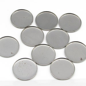 May include: Ten round, silver-colored metal discs, likely for crafts or jewelry making.
