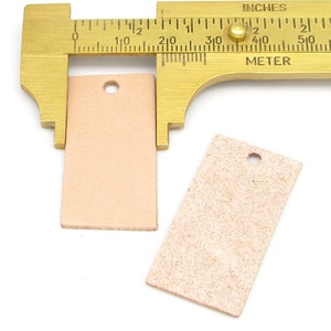 May include: Two rectangular leather tags with a hole punched in the top. The tags are measured with a brass caliper, showing the larger tag is 1.5 inches wide.