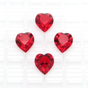 May include: Four red heart-shaped rhinestones on a white background.