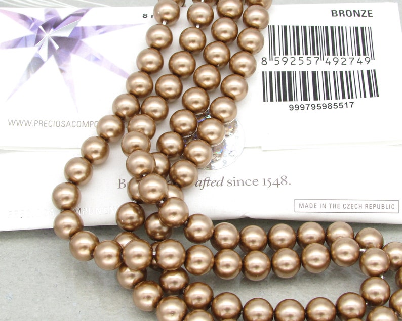 May include: A strand of bronze-colored round glass beads. The beads are approximately 8mm in diameter and have a smooth, shiny finish. The beads are strung on a clear thread and are ready to be used for jewelry making or other craft projects.