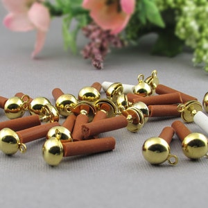 May include: A group of gold-colored metal bells with brown, cylindrical bases. The bells are arranged in a random pattern on a light gray surface.