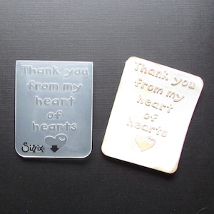 May include: A clear plastic embossing stencil with the text "Thank you from my heart of hearts" and a small heart design. The stencil is made by Sizzix.