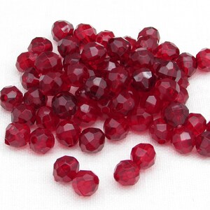May include: A collection of faceted, deep red beads. The beads have a multi-faceted design, catching the light and creating a sparkling effect. These beads are suitable for jewelry making and craft projects.