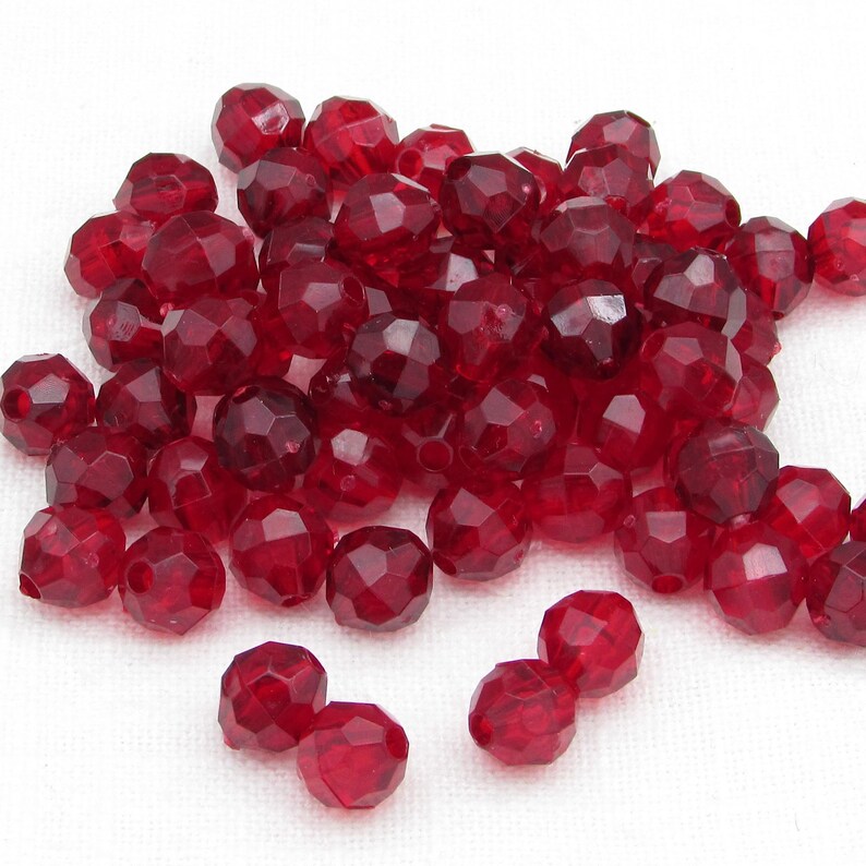 May include: A collection of faceted, deep red beads. The beads have a multi-faceted design, catching the light and creating a sparkling effect. These beads are suitable for jewelry making and craft projects.