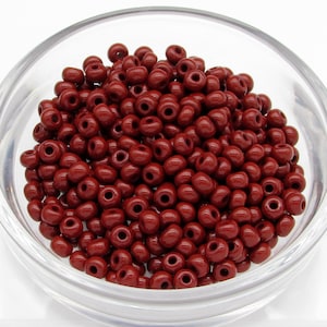 May include: A bowl filled with small, round, red beads. The beads are all the same size and shape, and they have a glossy finish.