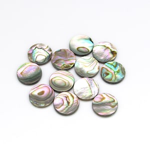 May include: A collection of 12 iridescent abalone shell round buttons. The buttons are a mix of light and dark colors with a pearlescent finish.
