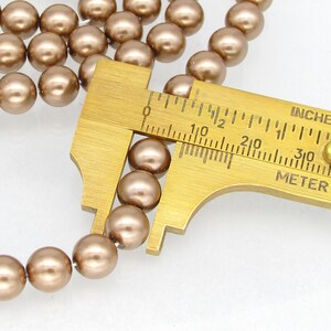 May include: A close-up of a strand of brown pearl beads being measured with a caliper. The caliper reads 1/2 inch or 1.27 cm.