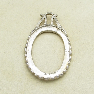 May include: Silver oval-shaped frame with a decorative top and beaded edge.