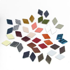 May include: A collection of small, diamond-shaped leather pieces in various colors, including blue, green, red, and white. Some pieces have textured patterns. These leather pieces are likely for crafting or embellishment.