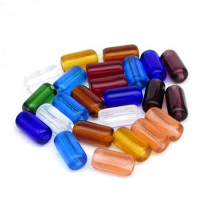 May include: A collection of cylindrical glass beads in various colors including blue, green, amber, red, purple, clear, and peach. Each bead features a smooth, polished surface and a rounded shape, arranged in a loose pile against a white background.