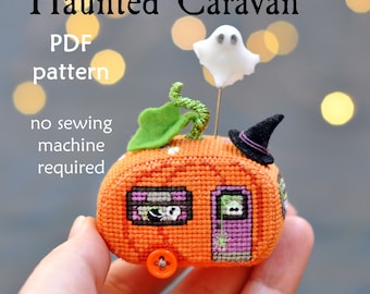 May include: A cross-stitch pattern for a haunted caravan shaped like a pumpkin. The caravan has a ghost, a witch's hat, and a green stem on top. The text on the image reads "Haunted Caravan PDF pattern no sewing machine required".