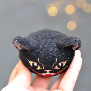 May include: A black knitted cat toy with embroidered yellow eyes and a red mouth.