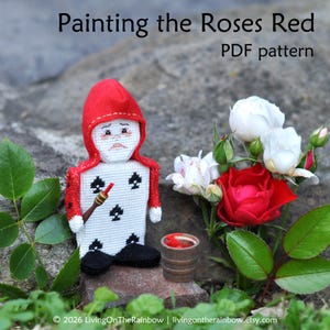 May include: A cross-stitch figure of a playing card character wearing a red hood, holding a small brush, standing next to a tiny wooden bucket of red paint and a cluster of white and red roses. Text reads: Painting the Roses Red PDF pattern.