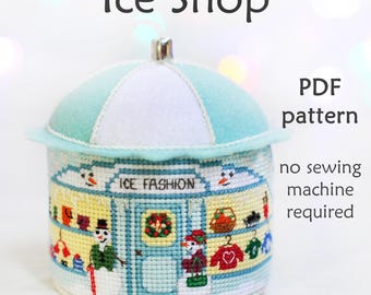 Può includere: Un modello PDF per un negozio di gelati in feltro con un tetto blu e bianco. Il negozio ha un cartello che dice "Ice Fashion" e presenta un pupazzo di neve e altri dettagli invernali. Non è necessaria una macchina da cucire.