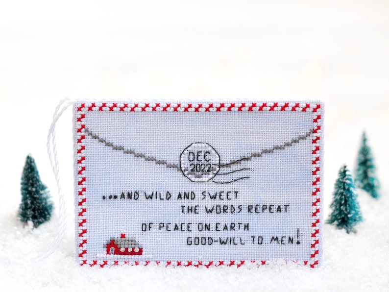 May include: A white cross-stitch ornament with a red border and a red house at the bottom. The ornament features a blue background with a gray envelope and a red stamp that says "DEC 2022". The text on the ornament reads "...AND WILD AND SWEET THE WORDS REPEAT OF PEACE ON EARTH GOOD-WILL TO MEN!"