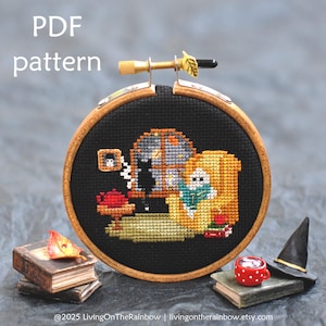 May include: A cross-stitch pattern in a wooden hoop, featuring a cozy scene with a black cat, a person, and a window. The text "PDF pattern" is at the top. The scene is surrounded by miniature books, a witch hat, and a red cup.