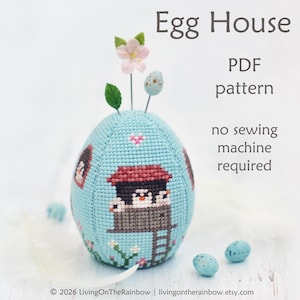 May include: A light blue egg-shaped craft with a cross-stitch design of a birdhouse and birds. The egg has decorative pins with flowers and eggs on top. The text "Egg House PDF pattern no sewing machine required" is also visible.