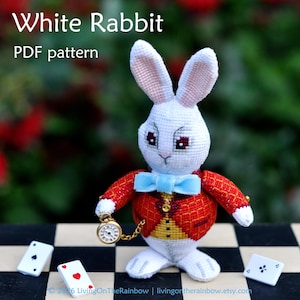 以下が含まれることがあります： クロスステッチで刺繍された白いウサギのフィギュア。赤い柄のジャケット、黄色いベスト、水色の蝶ネクタイを着用しています。ウサギはチェーン付きの金色の懐中時計を持っています。テキストはWhite Rabbit PDF pattern。近くに3枚のトランプが置かれています。