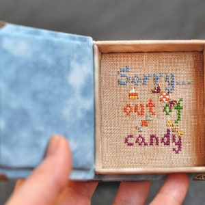 Pu&ograve; includere: Una piccola scatola rivestita in velluto blu con un coperchio incernierato. L'interno della scatola &egrave; rivestito in tessuto beige e presenta un ricamo a punto croce con la scritta "Mi dispiace, niente caramelle".