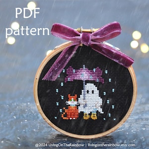 May include: A cross-stitch pattern featuring a ghost holding an umbrella over a cat in the rain. The pattern is stitched on black fabric and framed in a wooden hoop. The text "PDF pattern" is visible at the top of the image.