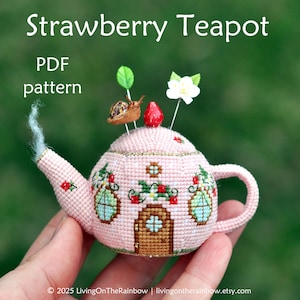Könnte beinhalten: Ein rosa Teekannen-Stecknadelkissen mit einer Erdbeere oben drauf, verziert mit einer Schnecke, Blumen und Fenstern. Die Teekanne ist von grünen Blättern und einer weißen Blume umgeben. Der Text "PDF pattern" ist auf dem Bild zu sehen.