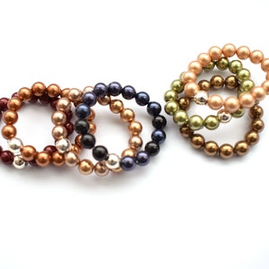 May include: A collection of beaded bracelets in shades of burgundy, bronze, gold, black, and navy. The bracelets are made with round beads and silver-coloured accents. They are displayed against a white backdrop.