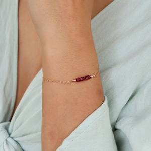 May include: A delicate gold chain bracelet with a small bar of red gemstones. The bracelet is made of 14k rose gold fill.