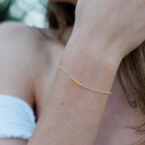 May include: A delicate silver chain bracelet with a small yellow gemstone charm. STERLING SILVER is written in the bottom left corner of the image.