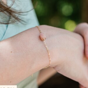 May include: A delicate gold chain bracelet with a single pink gemstone pendant. The bracelet is made of 14k gold fill.