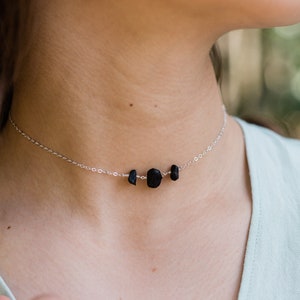 May include: A silver chain necklace with three black lava rock beads. The necklace is on a model's neck. STERLING SILVER is written at the bottom of the image.