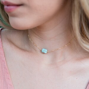 May include: A delicate gold chain necklace with a light blue gemstone pendant. The necklace is 14k gold fill.