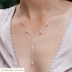 May include: A silver chain necklace with a delicate pendant and small pink beads. The necklace is layered with a shorter chain with pink beads.