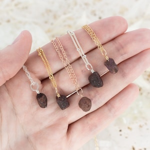 May include: Five necklaces with raw ruby pendants on gold and silver chains. The necklaces are displayed on a hand.