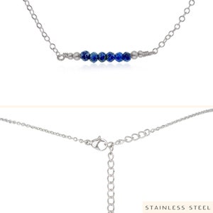 May include: A silver chain necklace with a row of blue gemstone beads. The necklace has a lobster claw clasp. "STAINLESS STEEL" is printed on the bottom of the image.