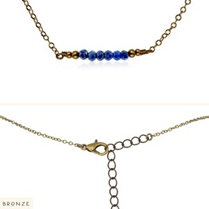 May include: A delicate gold chain necklace with a row of blue gemstone beads and a lobster clasp closure. The necklace is labeled "BRONZE".