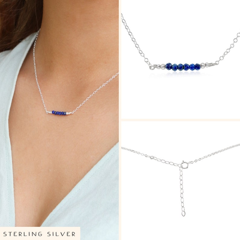 May include: A silver chain necklace with a row of small blue gemstone beads. The necklace is shown on a model wearing a light blue shirt. The necklace has an adjustable clasp.