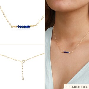 May include: A gold chain necklace with a row of small blue gemstone beads. The necklace has an adjustable clasp. 14K Gold Fill.