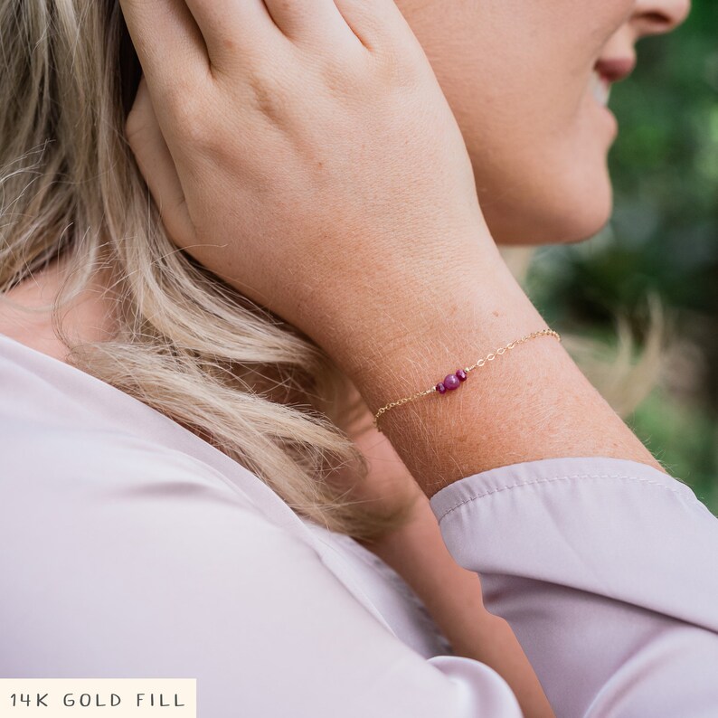 Puede incluir: Un delicado brazalete de oro con una cadena peque&ntilde;a y tres peque&ntilde;as piedras preciosas rojas. 14K Gold Fill.