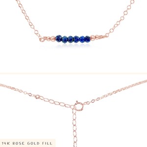 May include: A delicate gold chain necklace with a row of small, dark blue gemstone beads. The necklace is made of 14k rose gold fill.