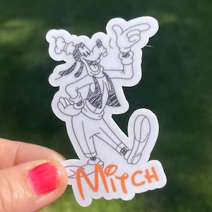 May include: A black and white line drawing of Goofy, a cartoon dog, wearing a hat and a bow tie. The drawing is on a white sticker with the name "Mitch" written in orange below the drawing.
