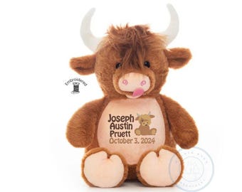 May include: A brown plush highland cow toy with white horns and a light pink muzzle. The chest features embroidered text reading Joseph Austin Pruett October 3, 2024, alongside a small cartoon cow graphic. The toy has shaggy fur and a pink tongue.
