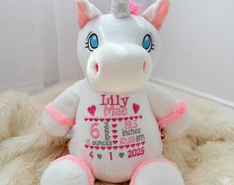 May include: A white plush unicorn toy with pink accents and a silver horn. The chest is embroidered with the name Lily Mae, birth details including 6 pounds 15 ounces, 19.5 inches, 10:59 am, and the date 4-1-2025, surrounded by pink heart motifs.